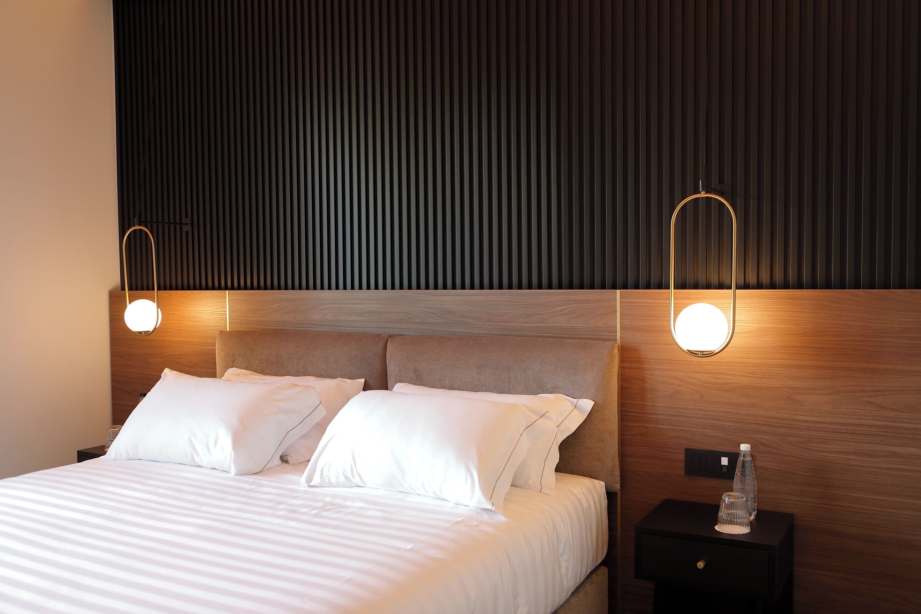 A neatly made bed with white linens, a wooden headboard, and two bedside lamps.