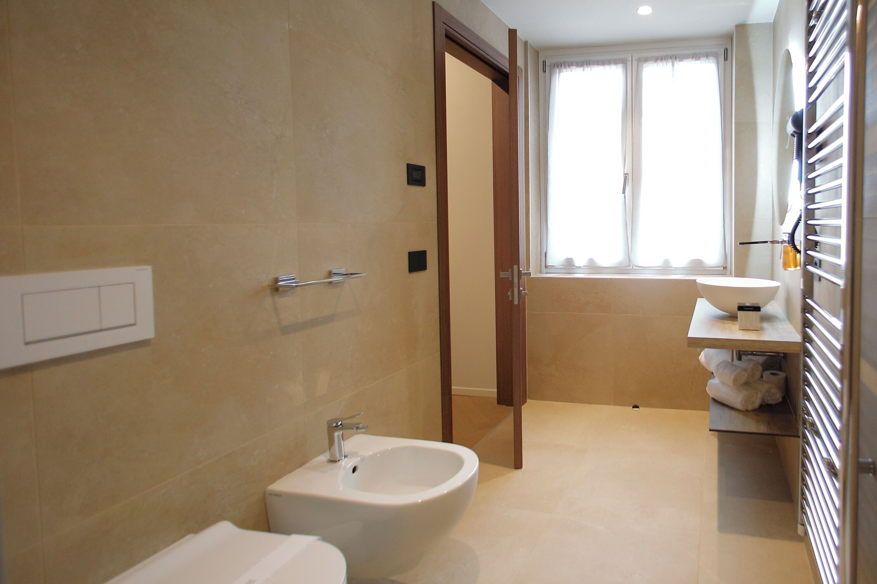 A bathroom with a bidet, a toilet, a towel rack, and a window with curtains.
