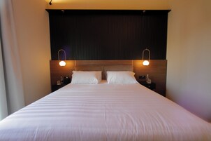 Una camera d'albergo con un letto grande, due comodini e una testiera scura.