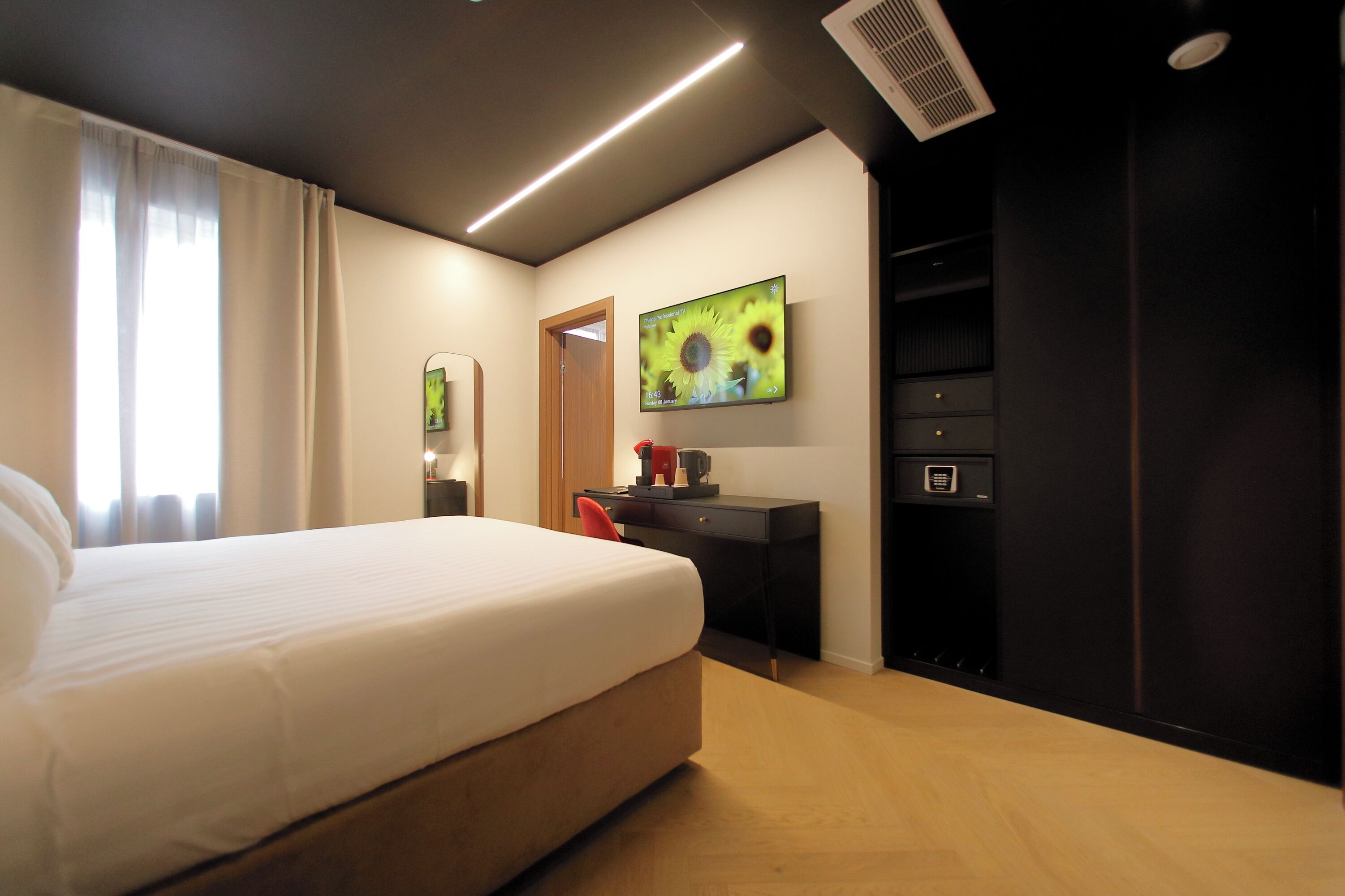 Una habitación de hotel con cama, escritorio, silla, televisor y armario.