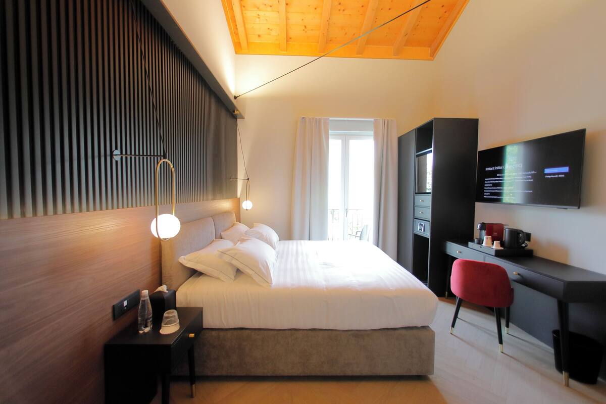 Une chambre d’hôtel moderne dotée d’un grand lit, d’un bureau avec une chaise, d’un téléviseur fixé au mur et d’une fenêtre avec des rideaux.