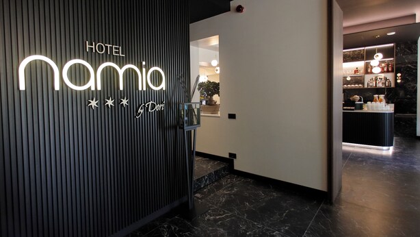 Ein Hotel mit moderner Gestaltung, ein Schild mit der Aufschrift "HOTEL namia" und ein Empfangsbereich mit Pflanze und Theke.