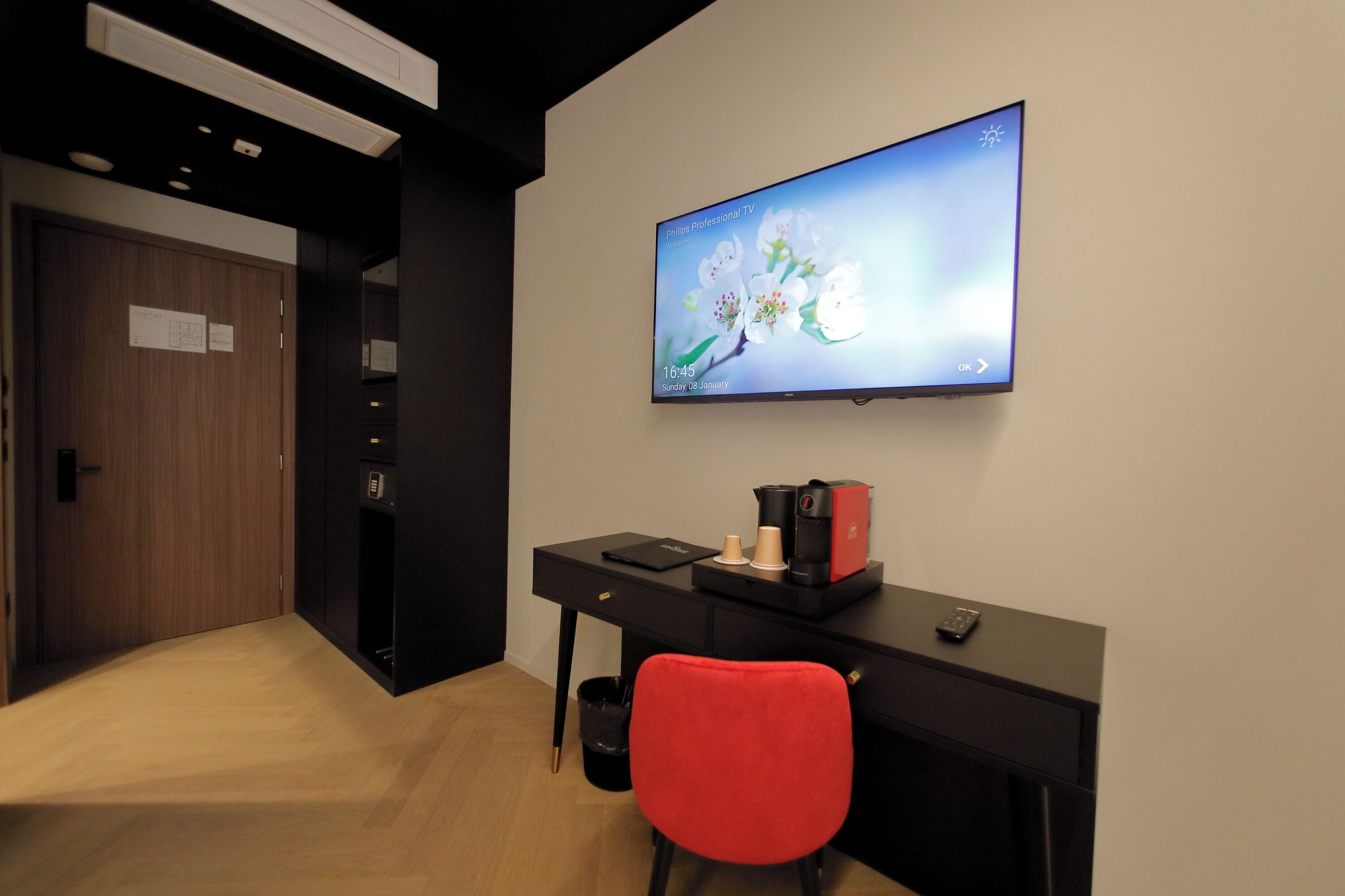 A modern office space with a black desk, a red chair, a coffee machine, and a TV displaying a floral wallpaper.