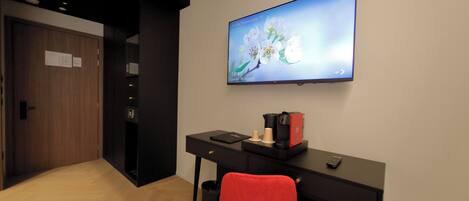 Un espacio de oficina moderno con un escritorio negro, una silla roja, una máquina de café y un televisor que muestra un papel tapiz floral.