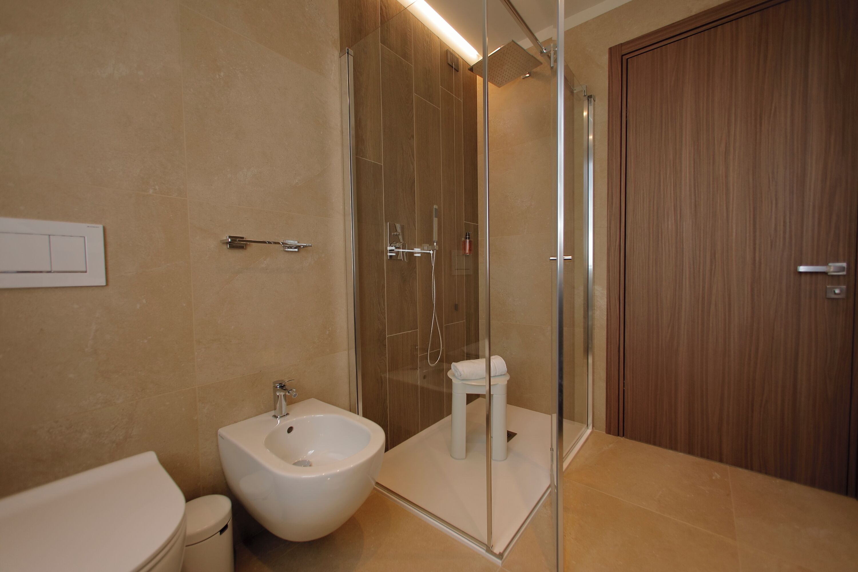 Une salle de bain moderne équipée d’un bidet, d’une douche à parois de verre et d’une porte en bois.