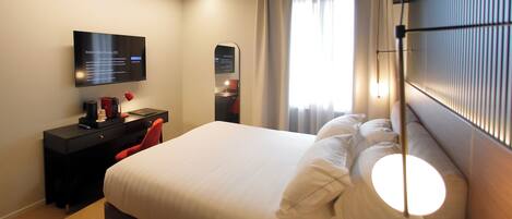 A modern hotel room with a large bed, a desk with a computer, a flat-screen TV, and a large window with curtains.