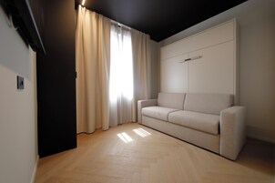 Una sala moderna con sofá, una ventana con cortinas y suelo de madera.