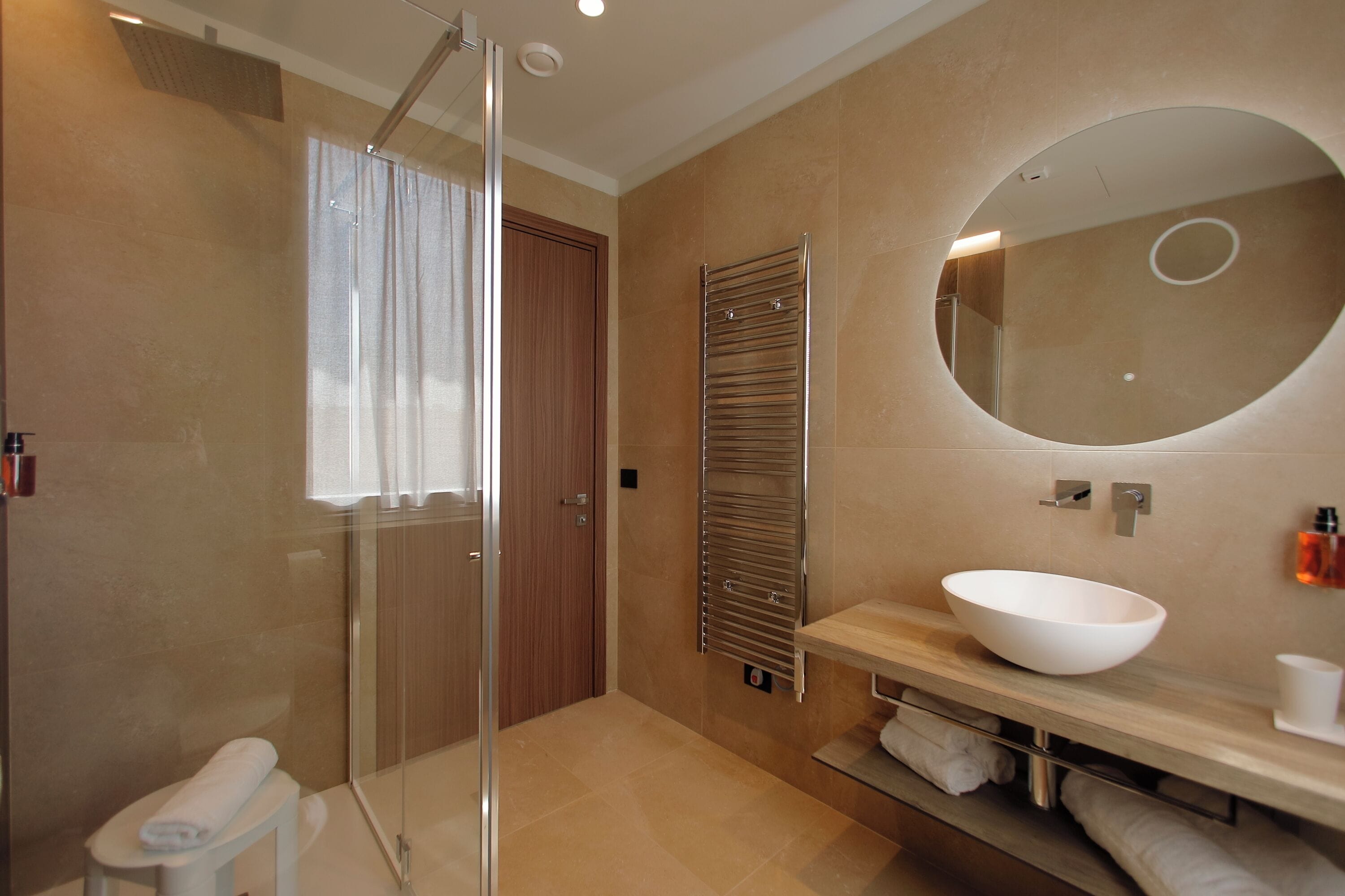 A modern bathroom with a glass shower enclosure, a wooden door, a large mirror, and a white sink.