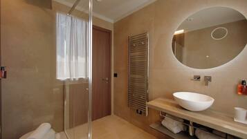 A modern bathroom with a glass shower enclosure, a wooden door, a large mirror, and a white sink.