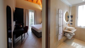 Ein Hotelzimmer mit Bett, Schreibtisch mit Stuhl, Fernseher, Badezimmer mit Waschbecken und Spiegel sowie einem Fenster.