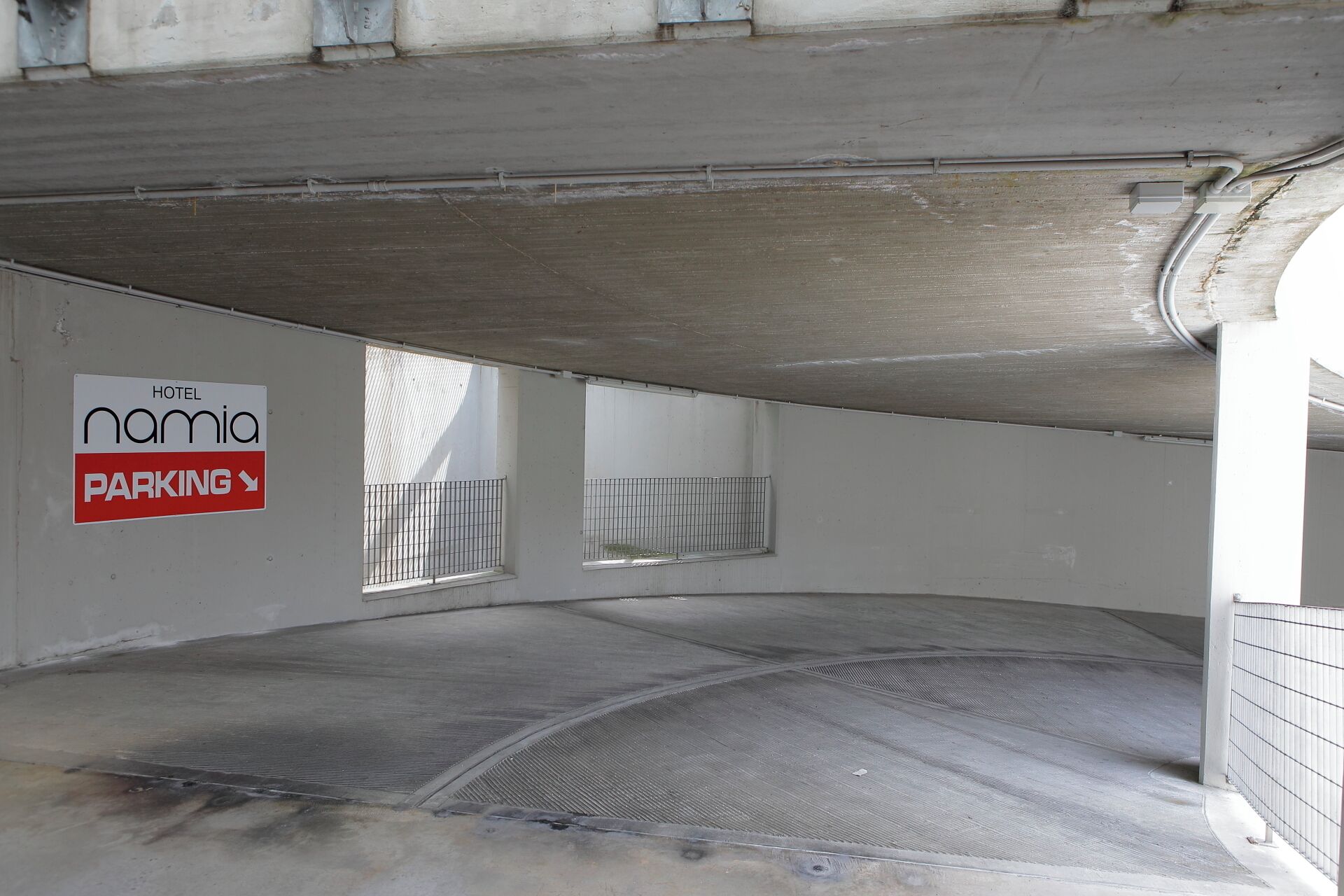 Un área de estacionamiento con un letrero que dice 'Hotel Namia' y una rampa metálica que conduce a un nivel superior.