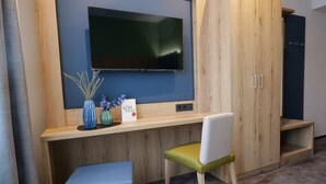 A modern room with a wooden desk, a television mounted on the wall, a chair, and a small bookshelf. - Reos Hotel Isny (Isny im Allgaeu)