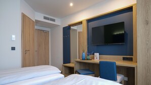 A hotel room with two beds, a desk, a chair, a TV, and a mirror. - Reos Hotel Isny (Isny im Allgaeu)