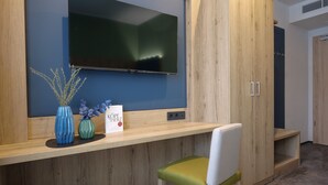 A modern room with a mounted TV, wooden furniture, and a small table with decorative items. - Reos Hotel Isny (Isny im Allgaeu)