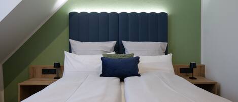 A double bed with white and blue bedding, two bedside tables with lamps, and a green accent wall.