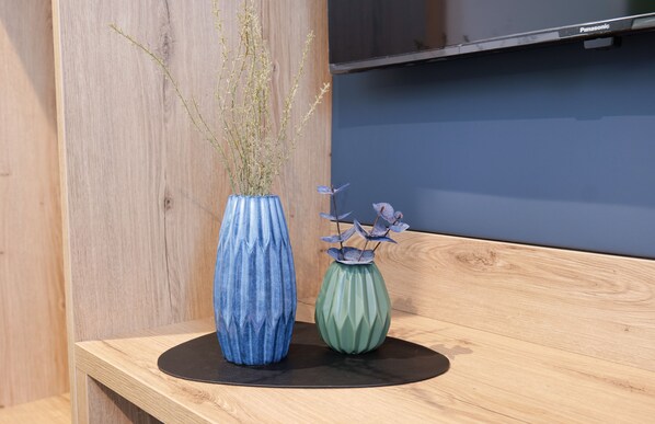 Dos jarrones con plantas sobre una mesa de madera, frente a un muro de madera y una pared azul.