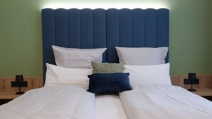 A neatly made bed with white linens, a blue headboard, and two bedside tables with lamps. - Reos Hotel Isny (Isny im Allgaeu)