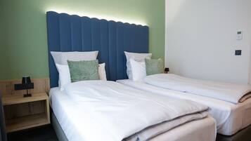 Habitación de hotel con dos camas individuales, una mesita de noche de madera con lámpara y una pared decorativa verde.