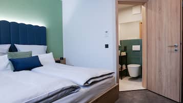 Una cama bien hecha con ropa de cama blanca y azul, cabecera de madera y una pared de acento verde.