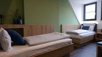 A bedroom with two wooden beds, a green wall, and a window.