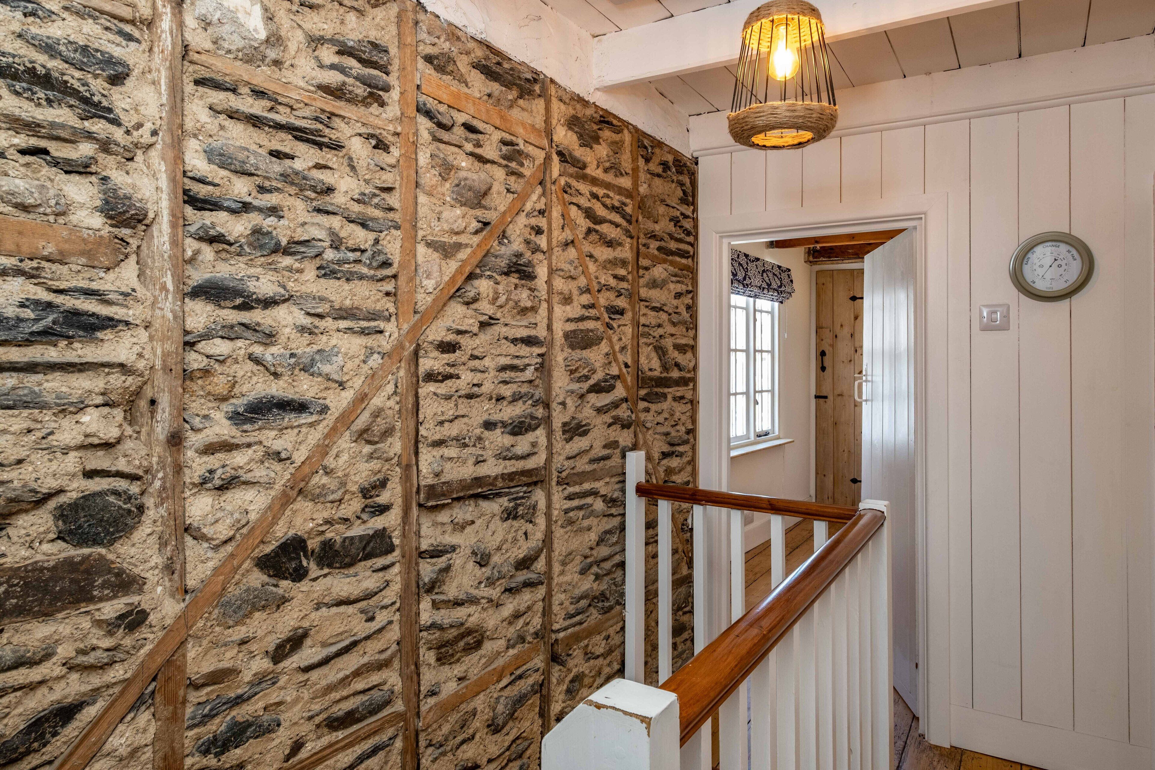 A staircase with a stone wall, wooden railing, and a hanging light fixture.