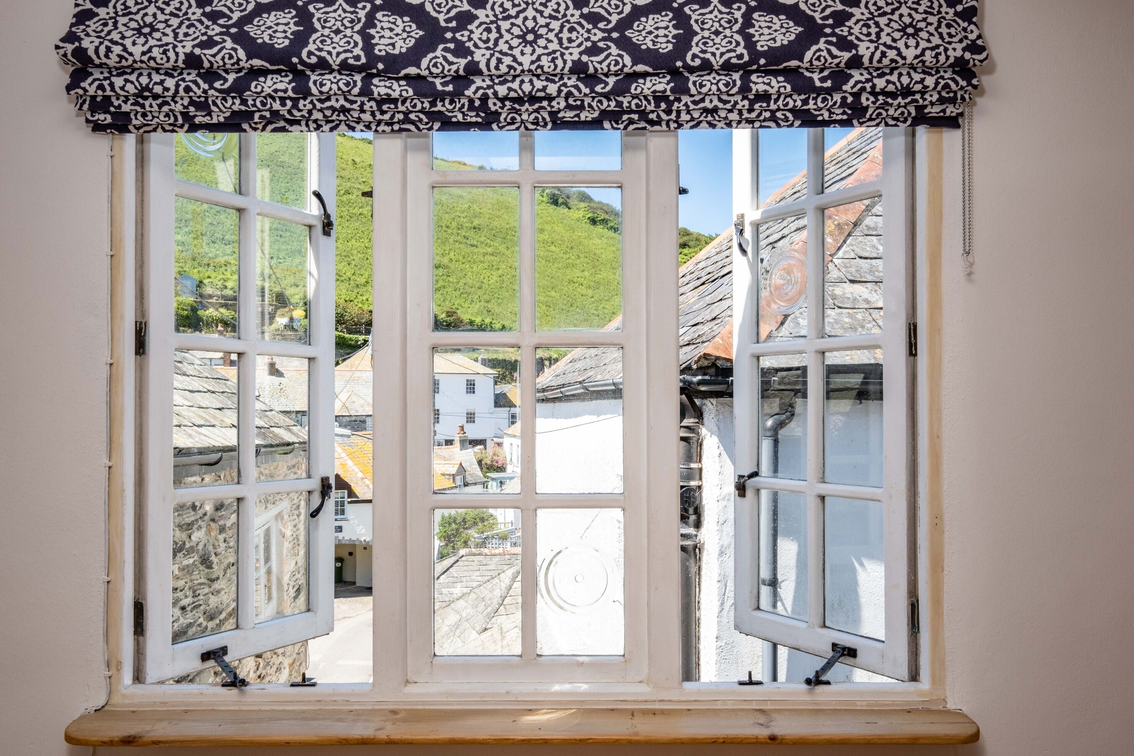 A window with a patterned valance, offering a view of buildings and a hill.