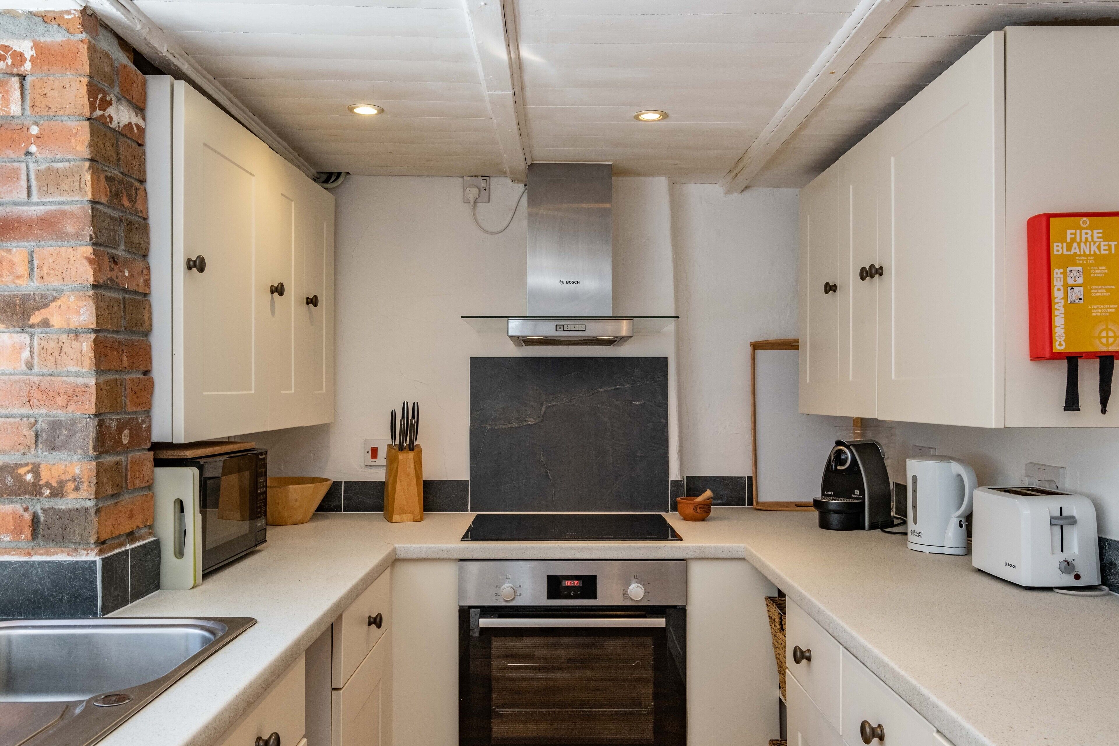 A kitchen with white cabinets, a Bosch range hood, a microwave, a toaster, and a fire blanket on the wall.