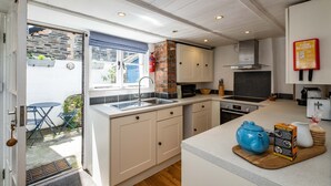 A modern kitchen with a large island, white cabinetry, and a fire blanket on the wall. - Sea Horses (Port Isaac)