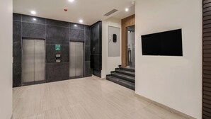 Un área de ascensores moderna, con dos ascensores, una escalera y un televisor montado.