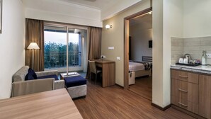 Habitación de hotel con balcón, escritorio, cama, kitchenette y zona de estar.