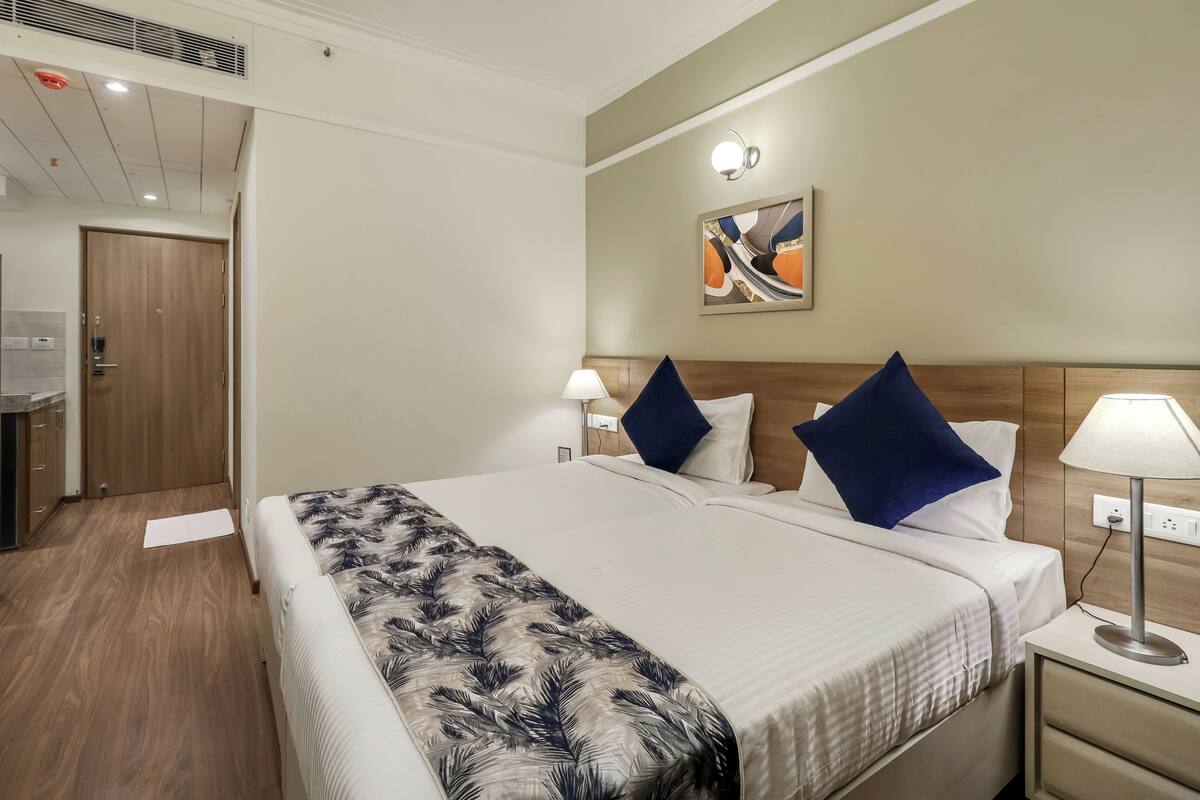 Ett hotellrum med en säng, sänglampor, ett nattduksbord, ett konstverk som hänger på väggen och en dörr av trä.