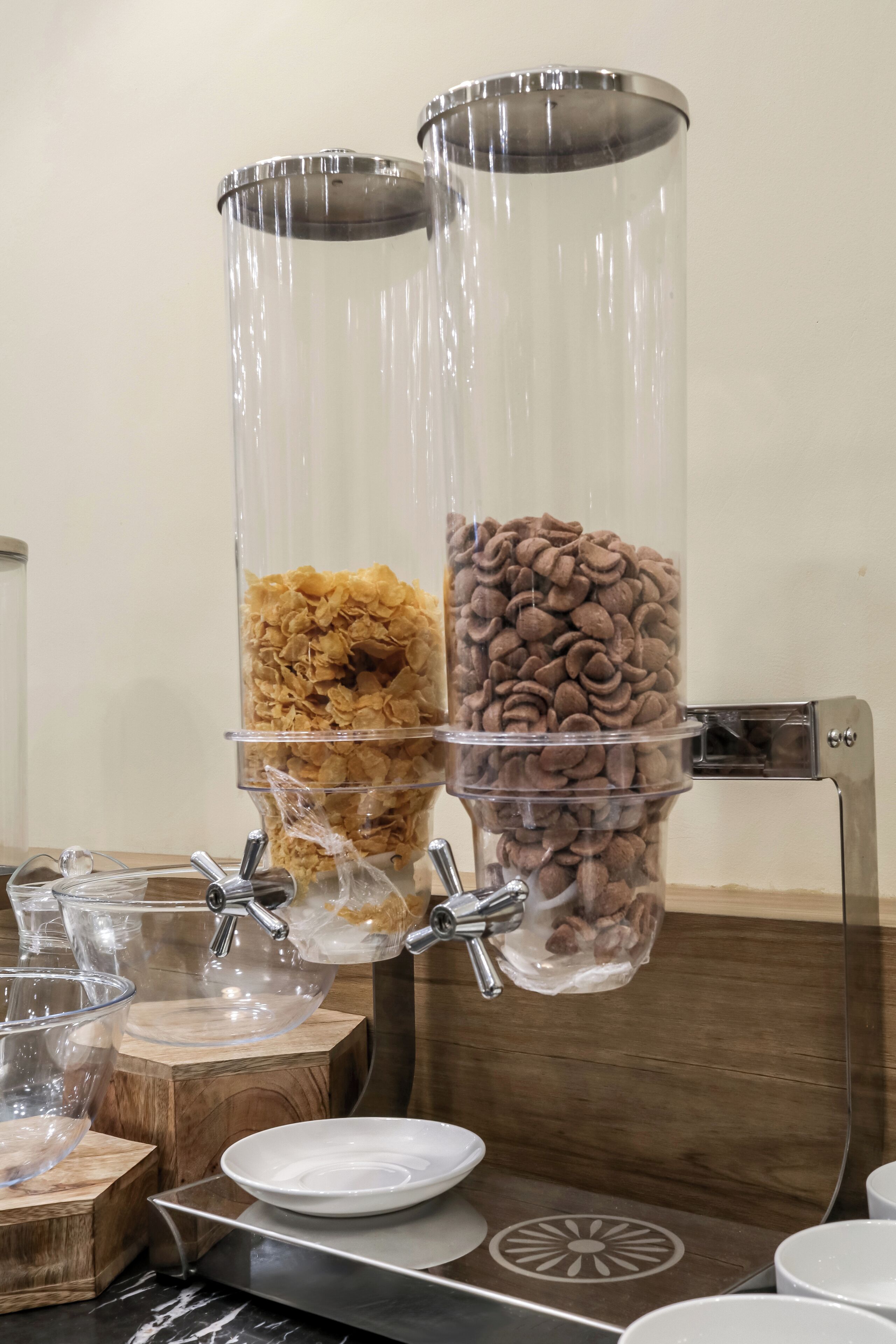 A beverage dispenser with two clear containers, one with orange cereal and the other with brown cereal.