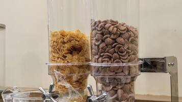 A beverage dispenser with two clear containers, one with orange cereal and the other with brown cereal.