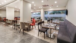 Un restaurante espacioso con varias zonas de comedor, incluyendo una mesa común alargada y varias mesas más pequeñas con sillas.