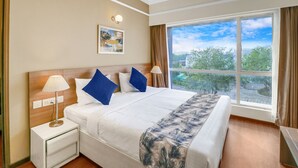 Habitación de hotel con una cama grande, una mesita de noche con lámpara, luz en la pared, ventana con vistas al exterior y ventilador de techo.