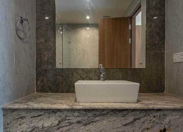 Un baño con lavamanos blanco, encimera de mármol y un espejo grande.