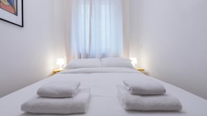 Ein ordentlich bezogenes Bett mit weißen Leinen und zwei am Fußende gefalteten Handtüchern.
