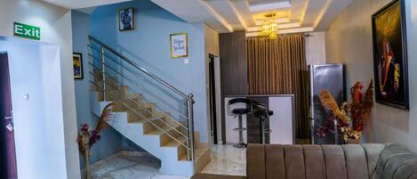 A modern hotel lobby with a marble floor, a staircase, a sofa, a refrigerator, and a bar area.