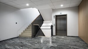 Un intérieur moderne avec un sol en marbre, un escalier doté de rampes noires et un ascenseur.