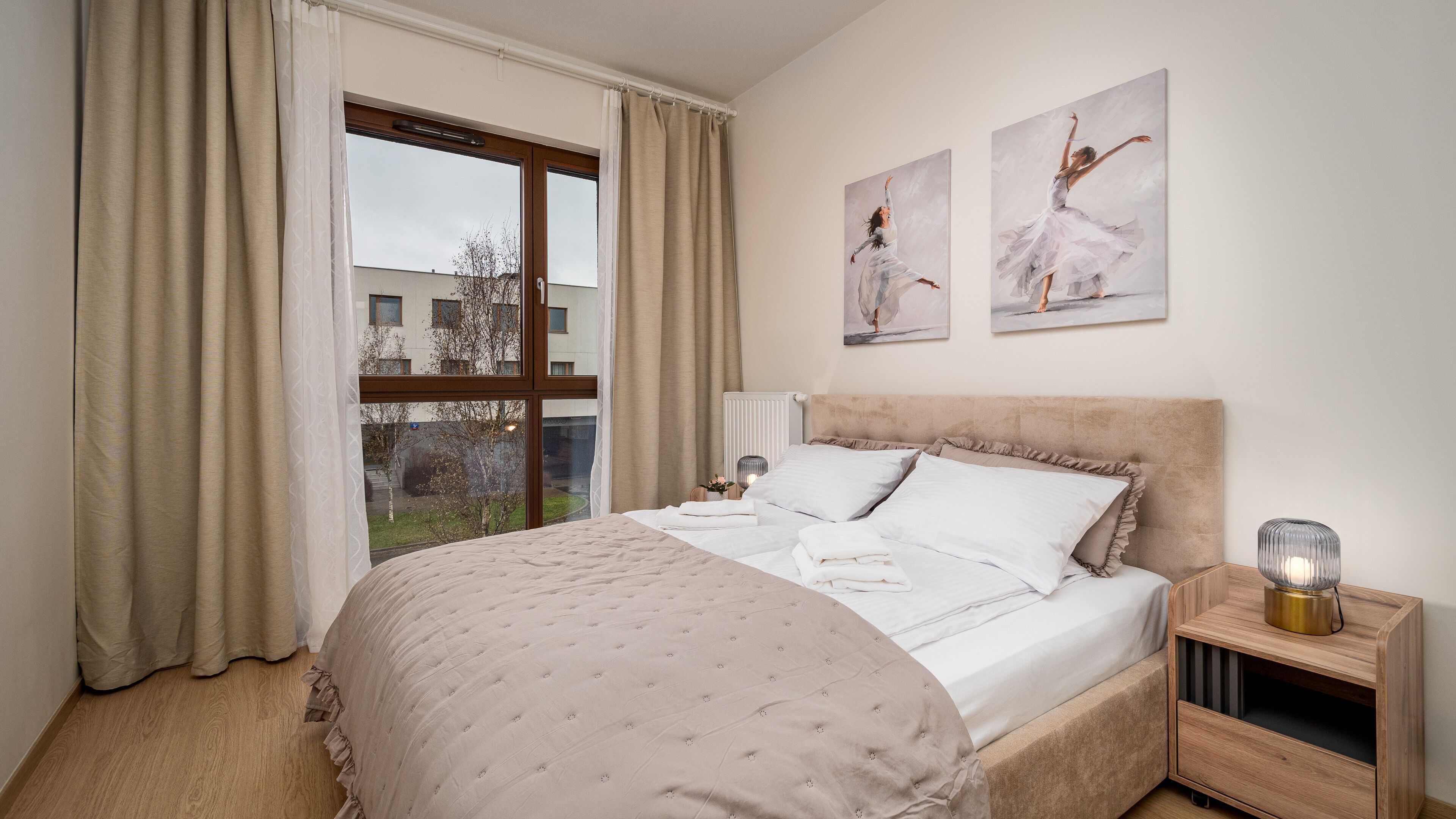 Habitación de hotel con una cama grande, una mesita de noche con lámpara y dos cuadros en la pared.