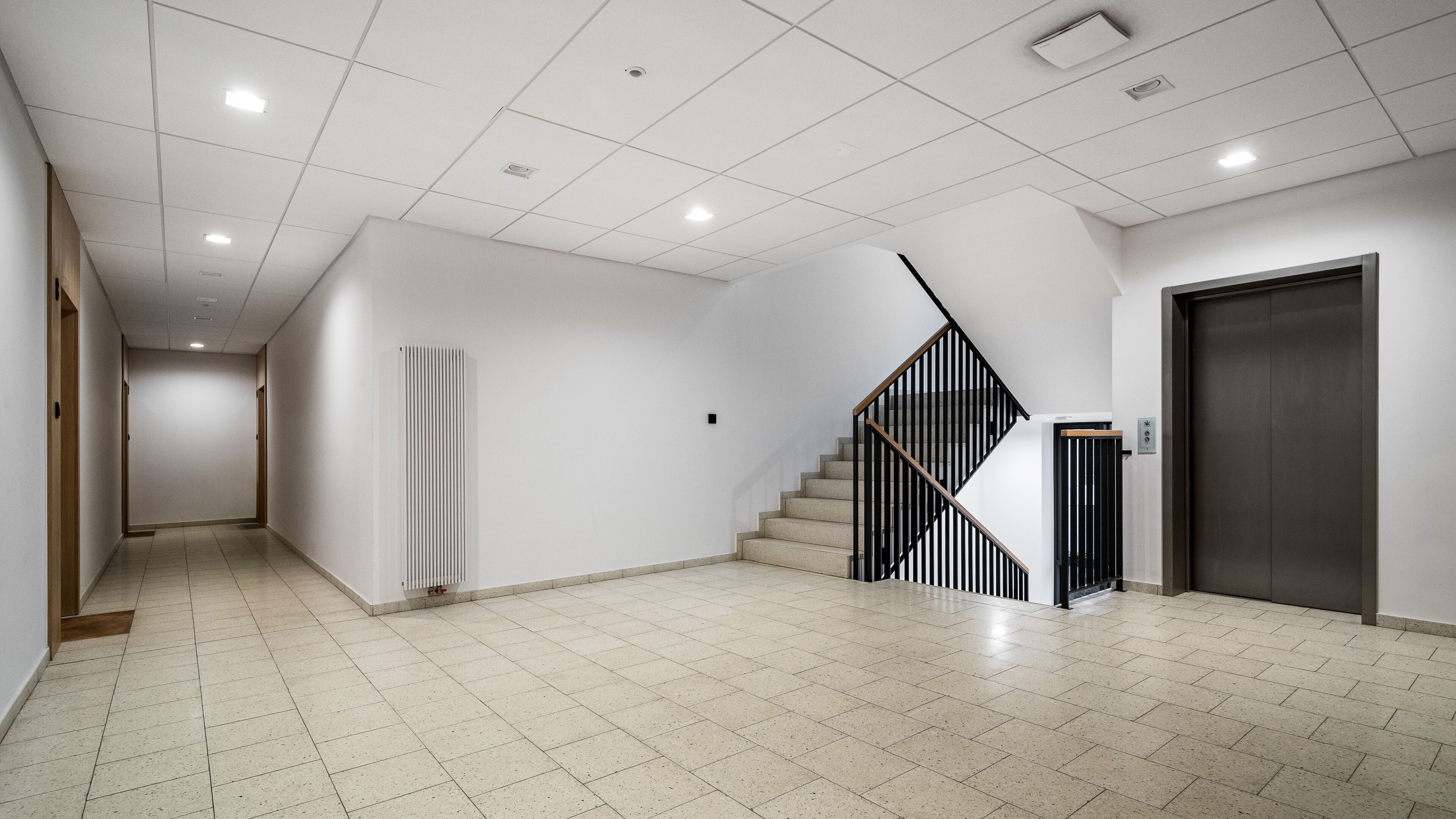 A spacious hallway with a modern staircase, a radiator, and a door.