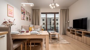 Un salon moderne comprenant un coin repas, un téléviseur à écran plat et une grande fenêtre donnant sur la ville.