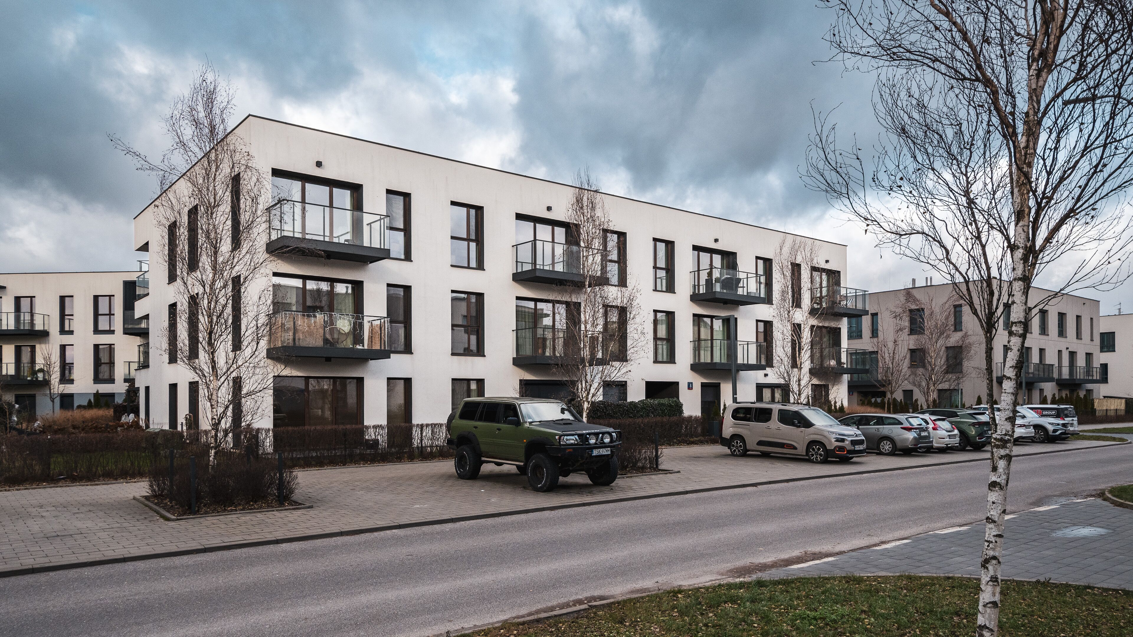Un immeuble résidentiel moderne à plusieurs étages, doté de balcons, avec des voitures garées et un ciel dégagé.
