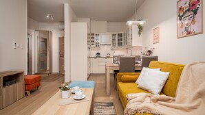 Un salon moderne avec un canapé jaune, une table basse avec des tasses, et un coin cuisine doté de placards et d’une table à manger.