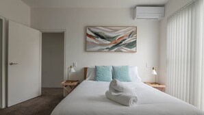 Siisti hotellihuone, jossa on huolitellusti pedattu sänky, taulu seinällä ja ikkuna, jossa on sälekaihtimet.