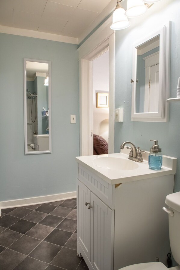 A bathroom with a white vanity, a sink, a mirror, and a toilet.