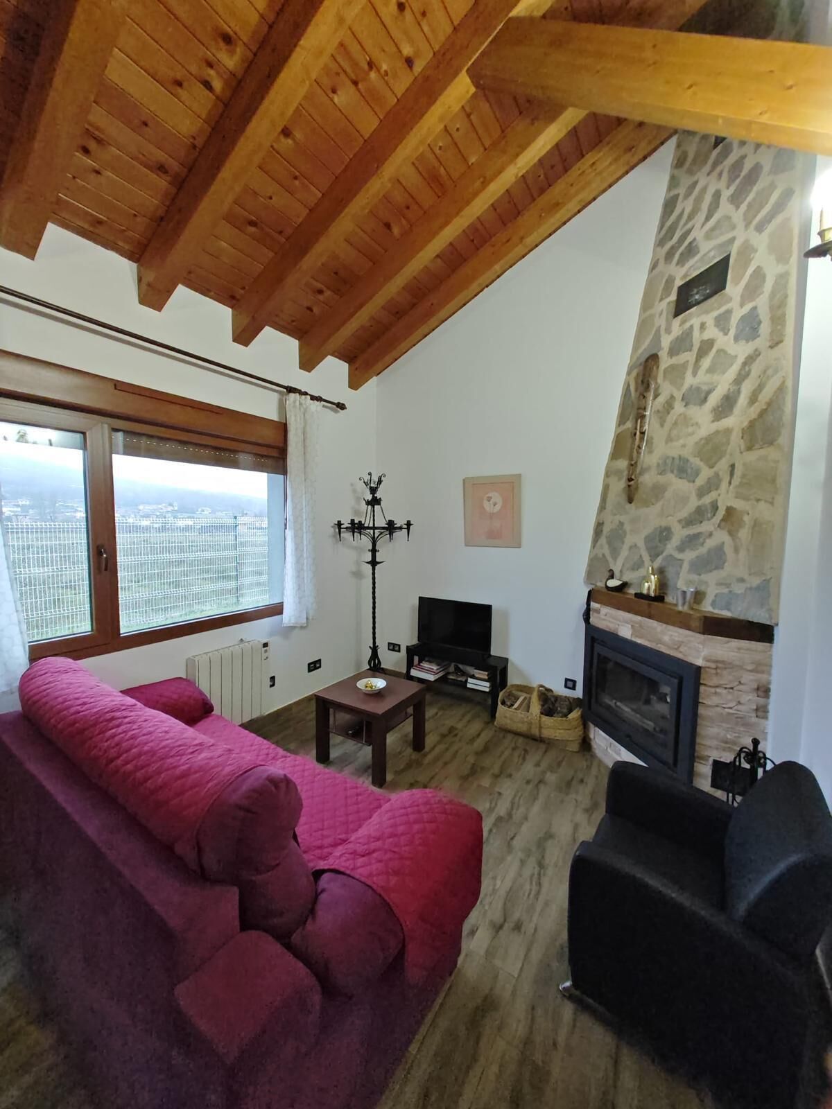 A cozy living room with a stone fireplace, a large window with a view, and a pink sofa.