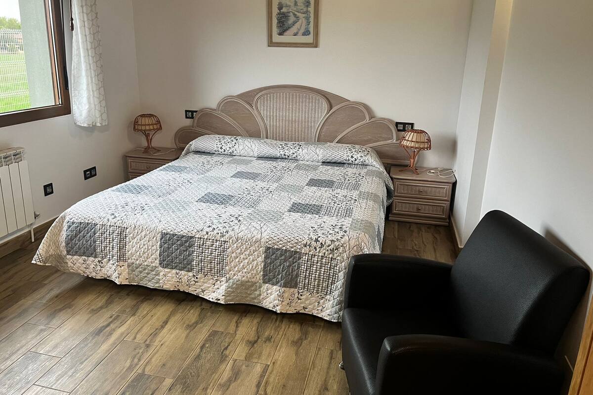 Une chambre à coucher avec un lit, une chaise, une table de chevet, une lampe et un tableau au mur.