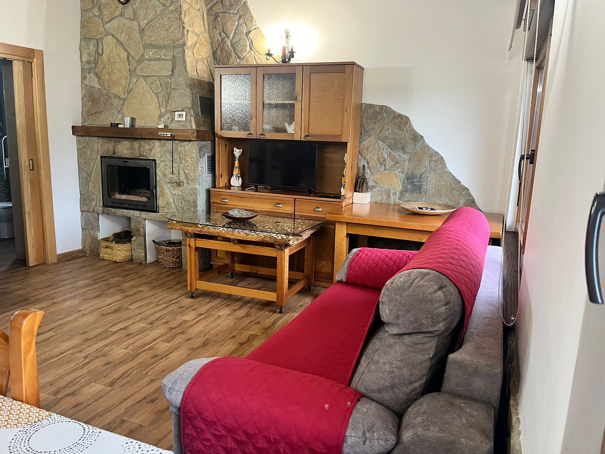 Zona d'estar acollidora amb una paret de pedra, una llar de foc, un televisor i un sofà vermell.