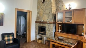 Un salon chaleureux avec une cheminée en pierre, un téléviseur et un meuble en bois.